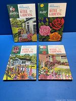 Four volumes of John Bradshaw's Better Gardening books, showing colorful illustrated covers featuring flowers and garden scenes, arranged on a blue background.