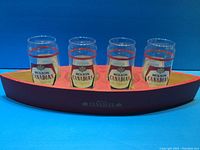Front view of four Molson Canadian glasses sitting in a red and black painted wooden canoe holder with Molson Canadian logo on the side