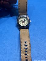 Front view of the vintage Mickey Mouse watch showing the dial with Mickey figure, beige leather strap, and metal casing.