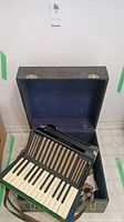 Hohner Student II accordion inside open hard carrying case with blue fabric lining, showing piano keys and straps.