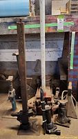 Photo showing four various car jacks including three mechanical screw jacks and a hydraulic floor jack, placed on a concrete floor by a wall.