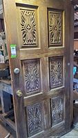 Front view of hand carved wooden door showing six panels with ornate wood carving on four panels, two brass doorknobs on the left side.