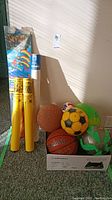 View of various balls in a box, yellow tubes and kite package in background
