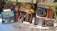 Overview of tools on bench including electric drill, chisels, large drill bits, tool belt, welding cables, and Milwaukee screwdriver bit case.