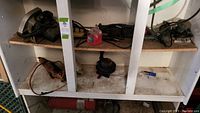 Shelf with various electrical tools including a red electrical motor or pump on bottom, and a dusty white shelf surface.
