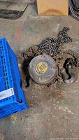 Close-up view of the Westward chain hoist on the floor with attached chains and hooks, showing wear and heavy use.