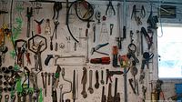 Wide view of many hand tools hanging on a white wall including wrenches, saws, pliers, and clamps, showing overall inventory and condition.