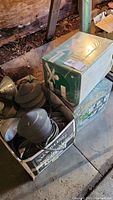 Box containing used outdoor electrical lights, visible cords and fixtures, placed on concrete floor.