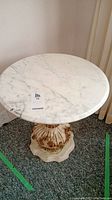 Top view showing round white marble tabletop with gray veining and a paper tag with item number.