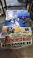 Metal beer posters including Molson Jack Hammer, Ski Genuine Bumps, Budweiser Genuine Draft, Budweiser Blue with a motorcycle image; posters appear to be metal sheet signs, measuring approx. 32x16 inches.