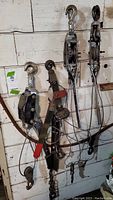 Four metal pull alongs hanging on wall composed of hooks, levers, pulley wheels, and wire cables for pulling or lifting.