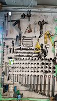Full view of wall mounted hand tools with socket wrenches, open-end wrenches, adjustable wrenches, scissors, pliers, and measuring tools organized and mounted on white board.