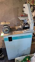 Side view of the Brice band saw on a wheeled homemade cart with the bench grinder beside it.