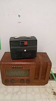 Vintage wooden radio with frequency display and control knobs alongside Keystone Dual 539 projector on top