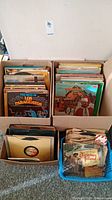 Four boxes of vintage records from assorted genres including Latin music, Christmas albums, and children's records, shown from a higher angle.