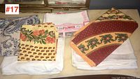 Six assorted vintage table cloths folded and stacked on a table showing various floral and stripe patterns.