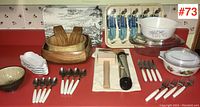 Full view of the assorted lot showing wooden bowls, Pyrex bowls, cutlery with white handles, ceramic bowls, and metal serving trays