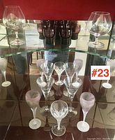 Overview of assorted vintage stemmed glasses with clear and frosted finishes, displayed on glass shelf