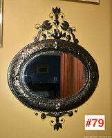 Full view of oval metal framed wall mirror hanging on yellow wall, showing reflective glass and decorative embossed frame.