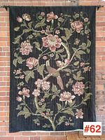 Full front view of the large wall tapestry hung on a brick wall showing floral and bird design.