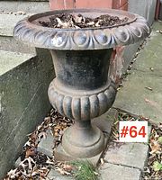 Full view of the vintage cast iron jardiniere planter showing overall shape and condition with soil and leaves inside.