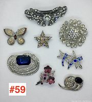 Full view of the 8 assorted brooches on white background showing overall lot contents, including the bow, butterfly, star, wreath, floral, dragonfly, oval, and circular designs.