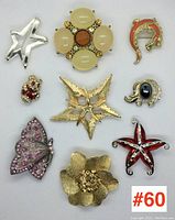 Group of 9 assorted costume brooches laid out on white background for full lot overview including star, flower, butterfly, dolphin, elephant, and others.