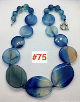 Full view of dyed blue agate necklace with large oval flat beads and smaller round beads strung on blue cord against white background.