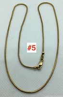 Snake chain necklace with lobster clasp laid in curved shape on white background