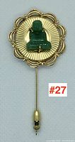 Front view of stick pin showing circular scalloped backplate, carved jade Buddha figure and pin stem