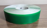 Side angle view of the green 3M tape roll showing its thickness and color, placed on a wooden surface.