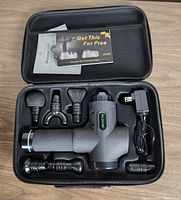 Open carrying case showing ALDOM massage gun, six interchangeable massage heads, charger, and promotional flyer.