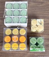 Photo of four packs of tealight candles in different colors and scents on wooden surface.