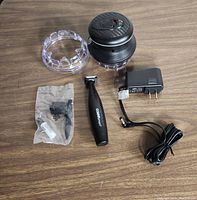 Cordless hair trimmer with removable protective cover, detail trimmer, charging adapter, and battery pack on a wooden surface.