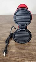 Red Dash Mini Maker open showing circular ridged grilling plates and attached power cord with plug