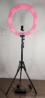Full view of the Fodoto 18 inch LED ring light mounted on an adjustable black tripod stand extending to 7 feet, showing the smartphone/camera mount in the center of the ring light and the power cable at the base.