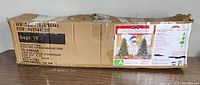 Distressed cardboard shipping box with label and product information of Holiday Time 6.5 ft pre-lit Sonoma pine tree for sale.