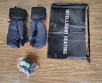 Pair of black heated gloves with integrated control, charging adapter in sealed packaging, and black carry case with Intelligent Heating branding