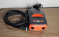 Skettle electric SUP pump in black and orange with hose accessory on a wooden surface