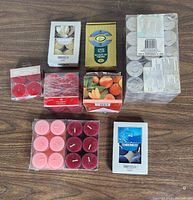 Overview of various sealed packs of tea light candles in different colors and scents on a wooden surface.