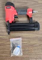 Workpro 18 gauge brad nailer with small accessories including a plastic bottle and 2 Allen wrenches on wooden surface