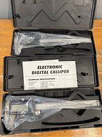 Two electronic digital calipers in open hard plastic cases with foam inserts, instruction sheets included.