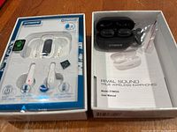 Photo showing two sets of Fisher wireless earphones side by side, one opened with case/manual and one sealed in original packaging.