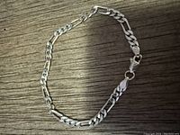 Silver chain bracelet laid flat showing the mix of Figaro and elongated links.
