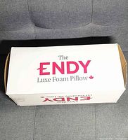 White box labeled 'The Endy Luxe Foam Pillow' on top and sides, displayed on gray couch.