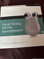 Front view of facial toning device box showing product image, name, size, and highlights microcurrent technology and FDA clearance.
