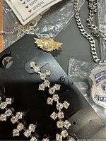 Photo of rhinestone drop earrings, gold-tone police wings pin, silver-tone chain necklace, and essential oil necklace.