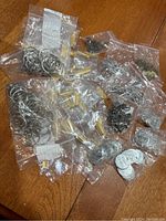 Top-down view showing multiple small bags of unused key rings and metal charms spread across a wooden table.