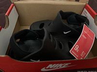 Top angled view of black Nike toddler sandals inside Nike branded box, size 9c tag attached