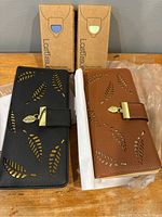 Two new wallets with leaf cut-out designs in black and brown, two last tissue handkerchief packages behind them